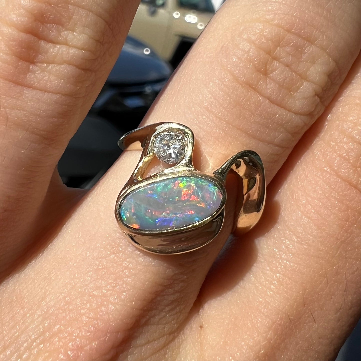 A ladies' yellow gold, bezel set ring mounted with a natural 1.15 carat black opal and round diamond.