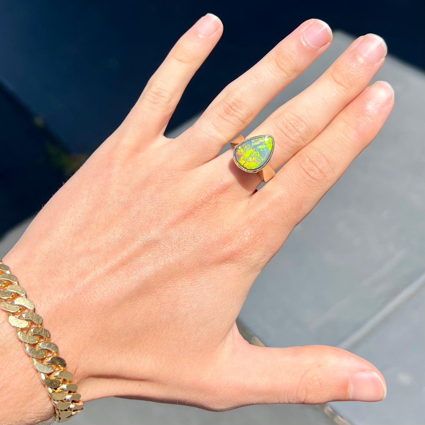 A large ladies' yellow gold solitaire ring set with a natural, pear shaped black crystal opal.  The opal has green and orange fire.