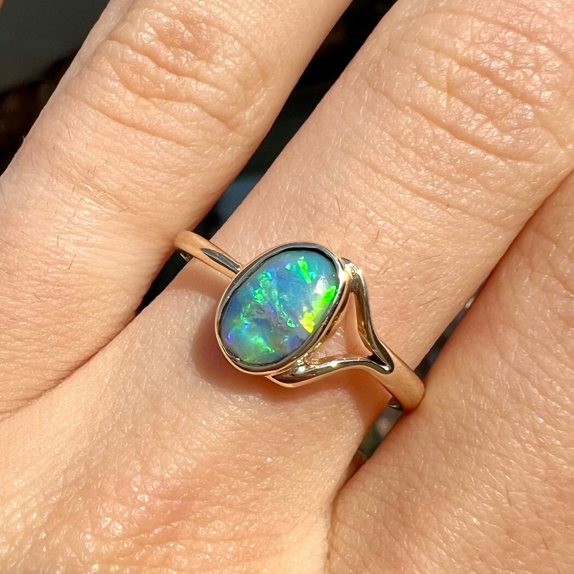 A ladies' oval cut black crystal opal solitaire ring handmade with a single split shank in yellow gold.