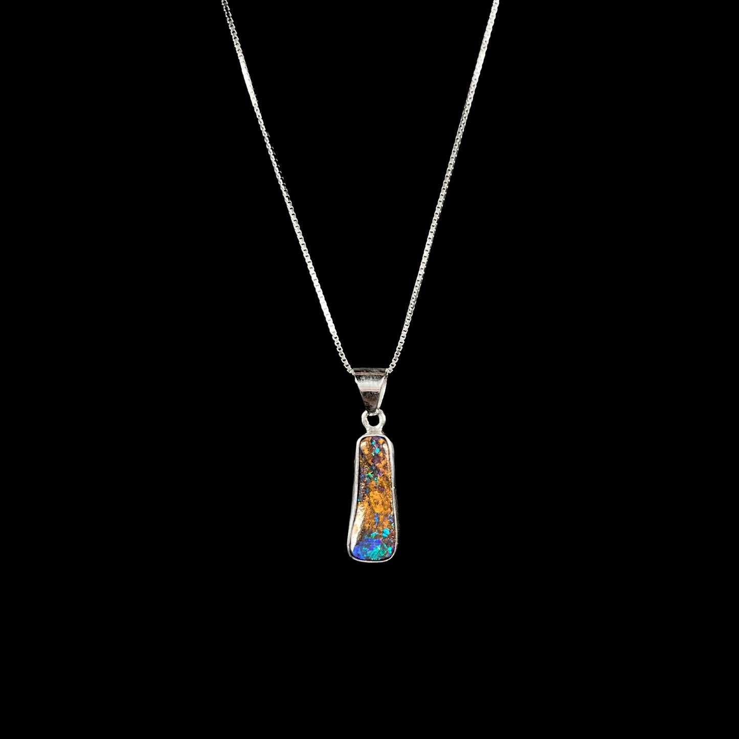 A sterling silver necklace bezel set with a natural Australian boulder opal stone.  The stone shines colors of blue, green, and purple.
