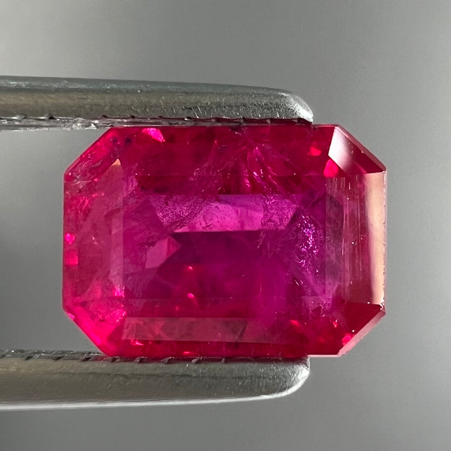 An emerald cut Burma ruby gemstone.  The stone is loose and a pinkish red color.
