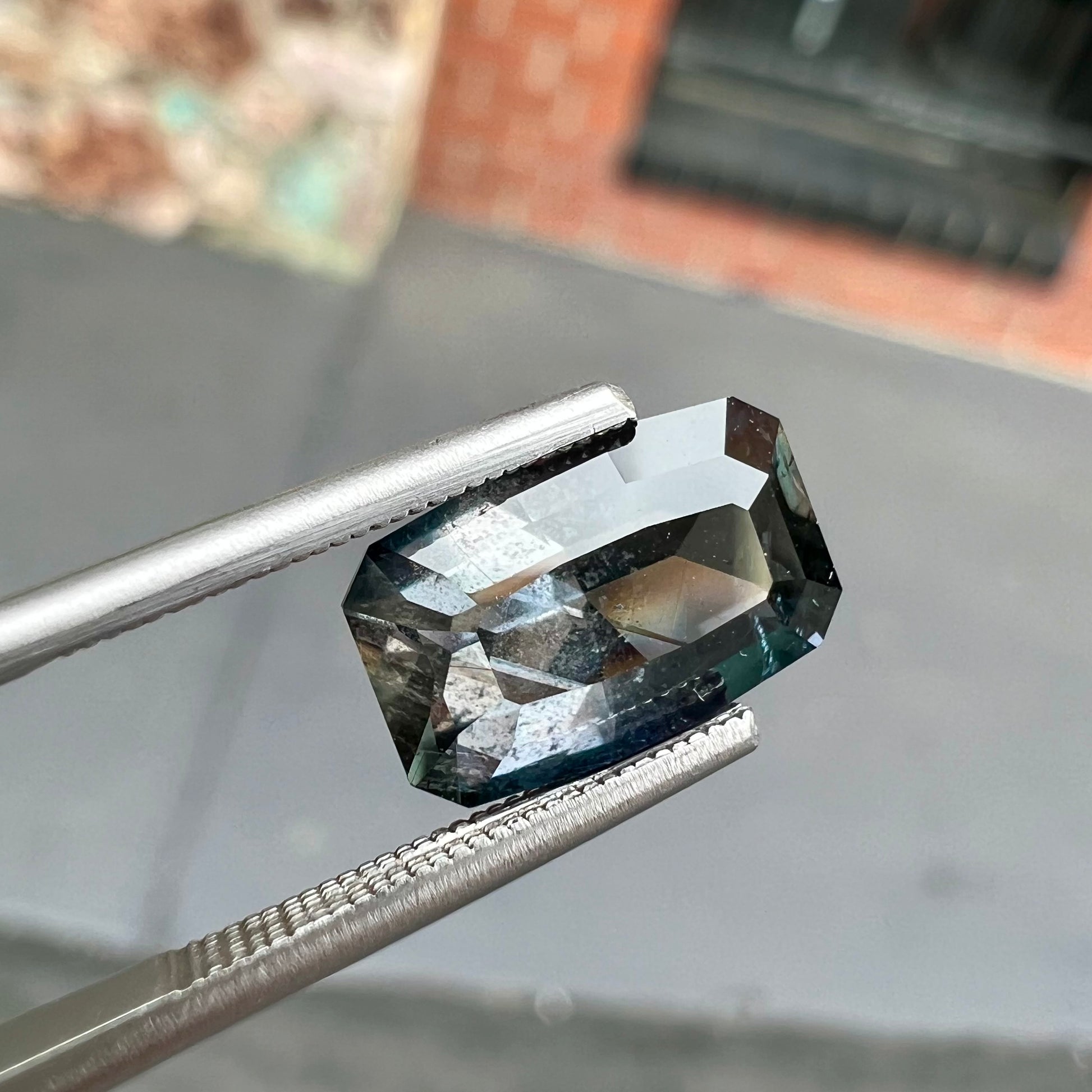 A loose, modified emerald cut, natural color change sapphire stone.  The stone shifts from black to blue to purple to green.