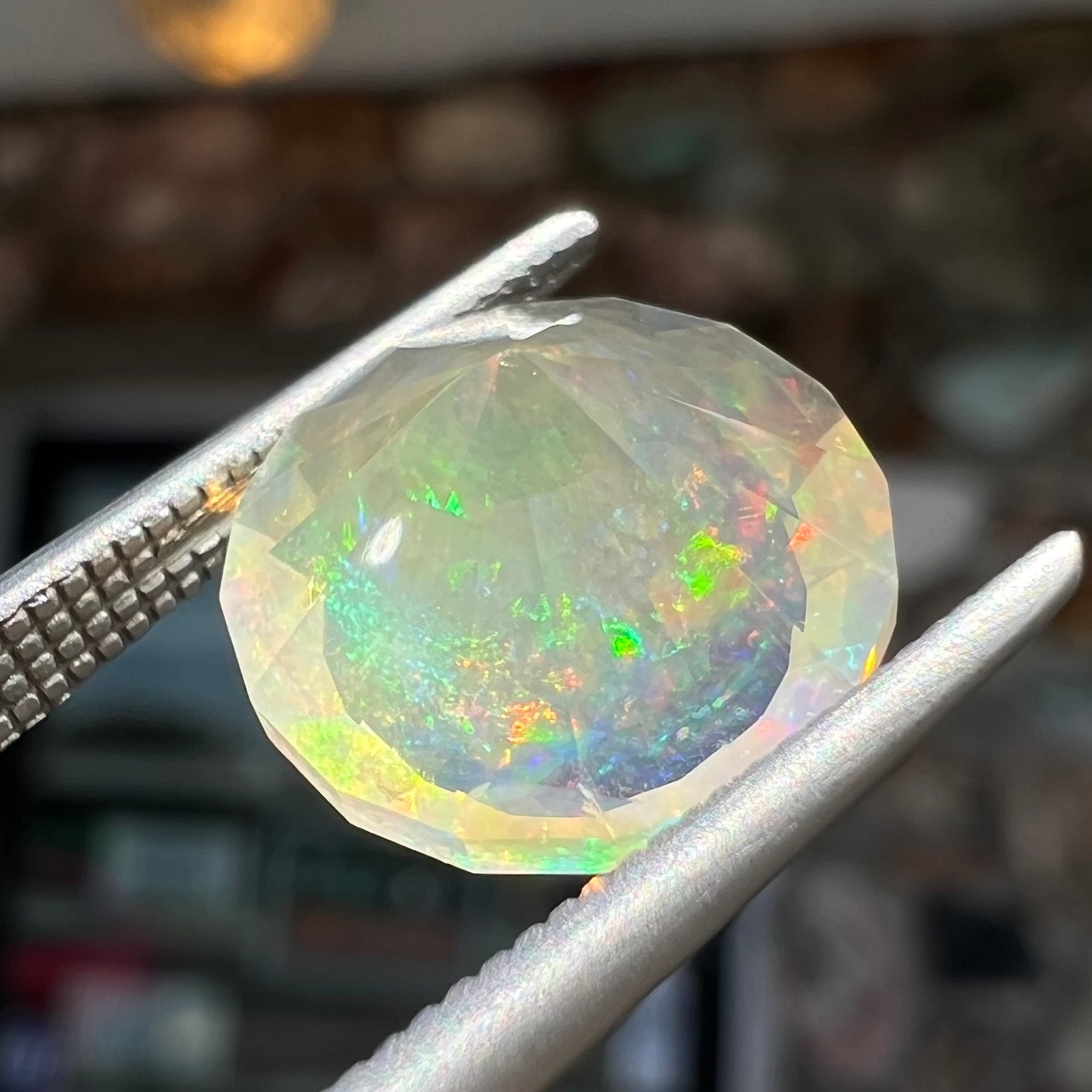A loose, round faceted Mexican fire opal gemstone.  The stone is transluscent light orange color with rainbow play of color in the sunlight.