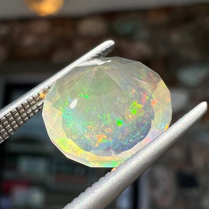 A loose, round faceted Mexican fire opal gemstone.  The stone is transluscent light orange color with rainbow play of color in the sunlight.