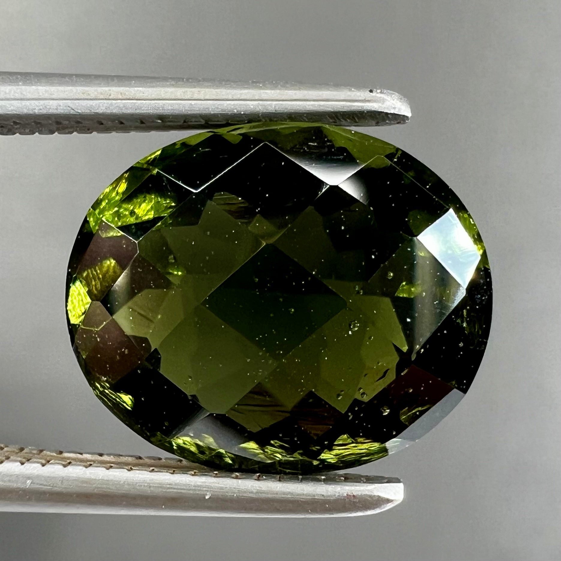 A loose, oval checkerboard cut natural moldavite gemstone.  The stone is dark green color.