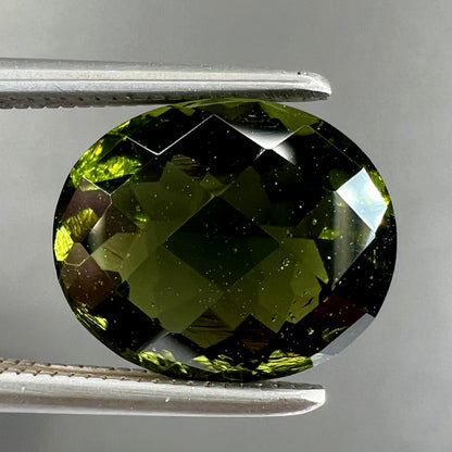 A loose, oval checkerboard cut natural moldavite gemstone.  The stone is dark green color.