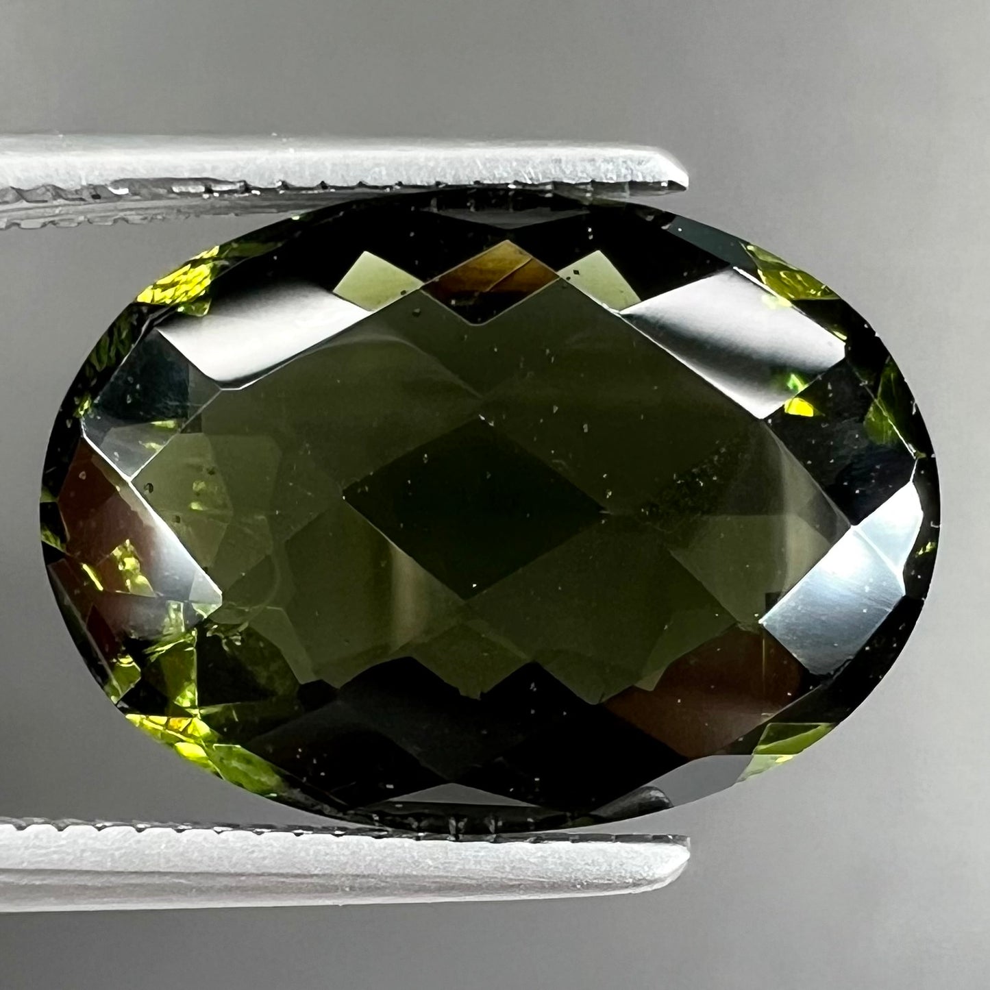A faceted oval cut natural moldavite gemstone.