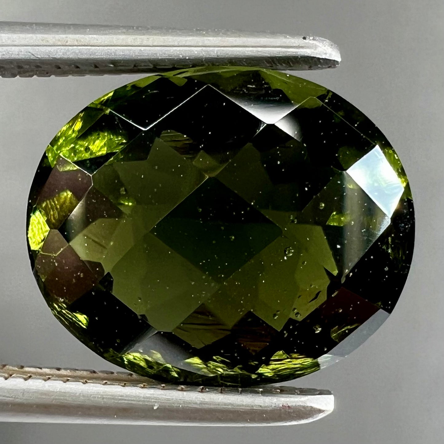 A loose, oval checkerboard cut natural moldavite gemstone.  The stone is dark green color.