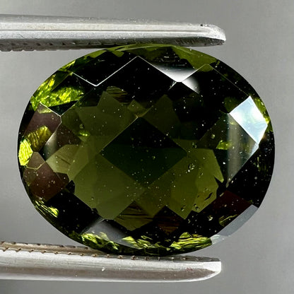 A loose, oval checkerboard cut natural moldavite gemstone.  The stone is dark green color.