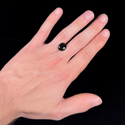 A loose, oval checkerboard cut natural moldavite gemstone.  The stone is dark green color.