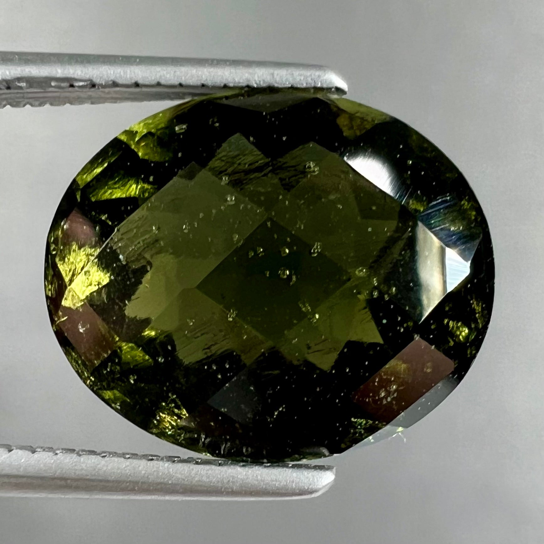 A loose, faceted oval cut natural moldavite gemstone.