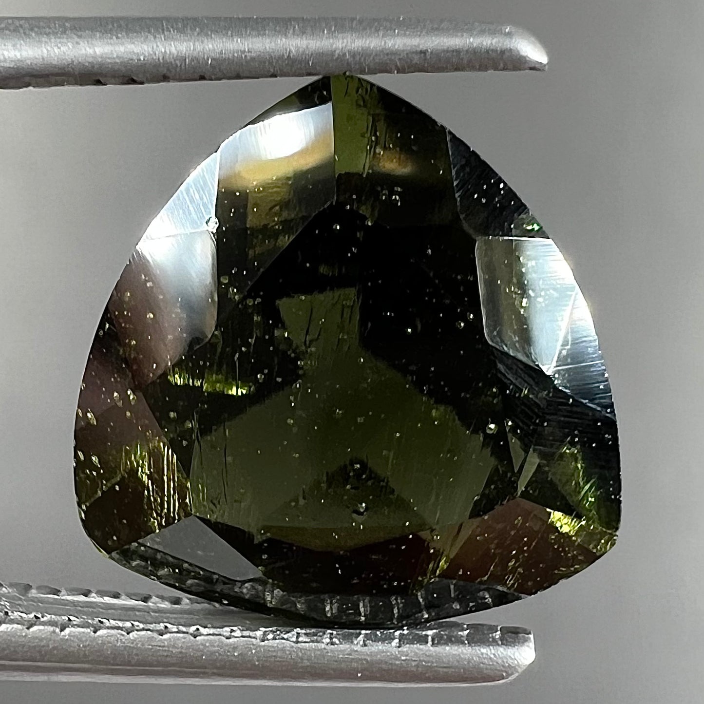 A faceted trillion cut natural moldavite gemstone that weighs 2.92 carats.  The stone is dark green color.