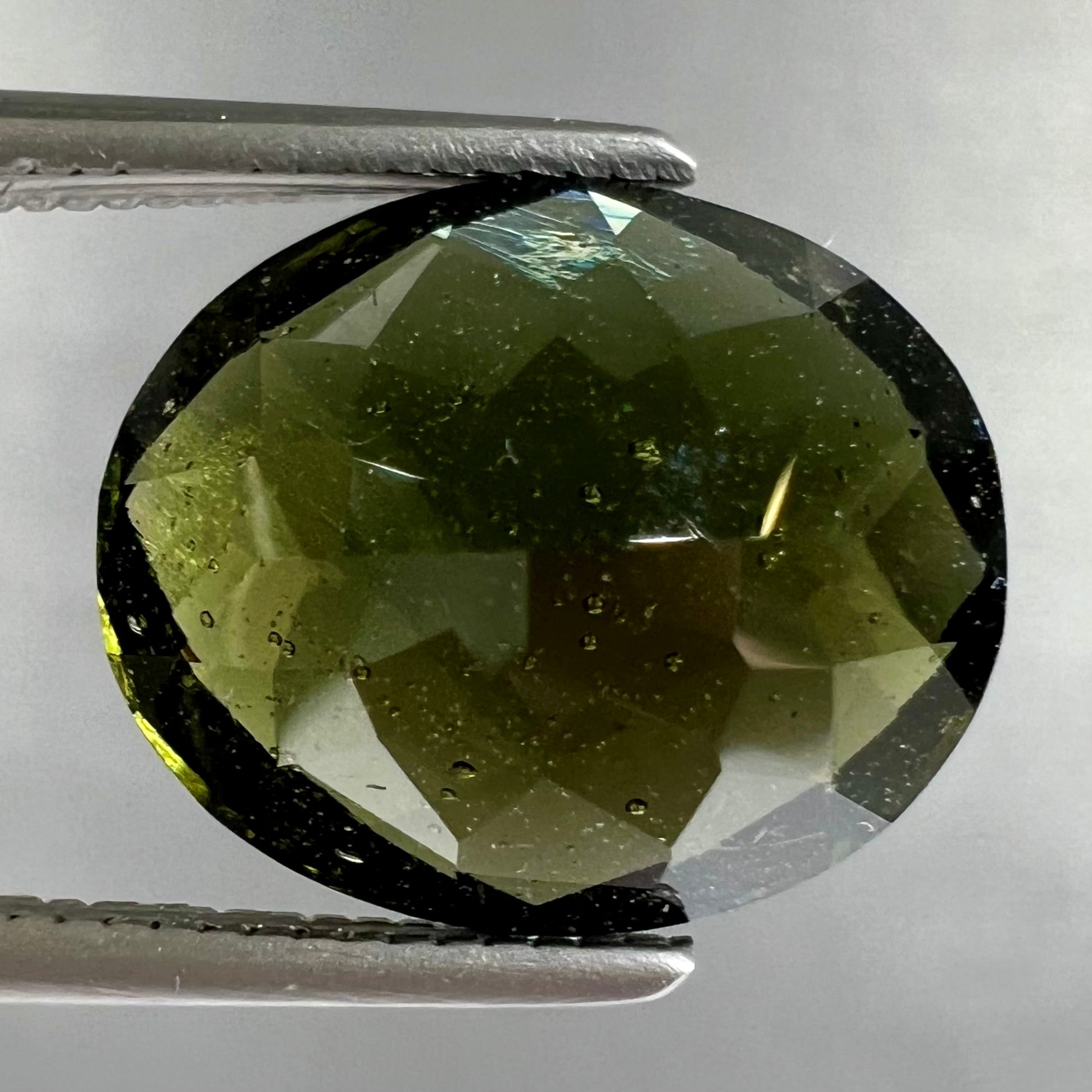 A loose, faceted oval cut natural moldavite gemstone.
