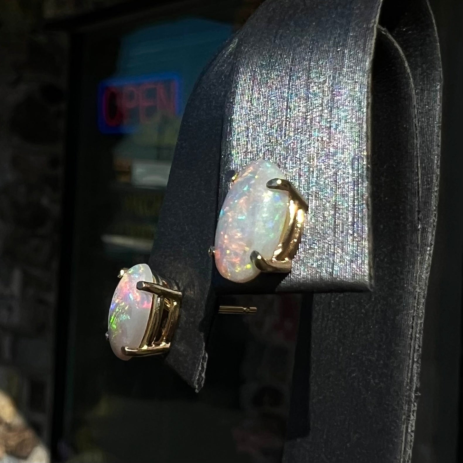 A pair of natural, semi-black crystal opal stud earrings in yellow gold.  The opals are oval cabochon cut.