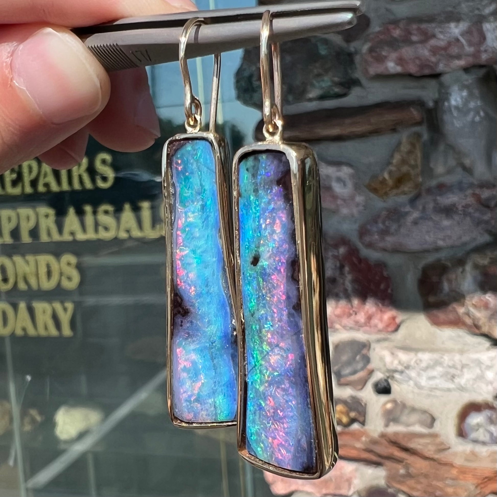 A pair of natural boulder opal dangle earrings set in yellow gold.  The opal displays a rainbow of colors and is from Bull Creek, Australia.