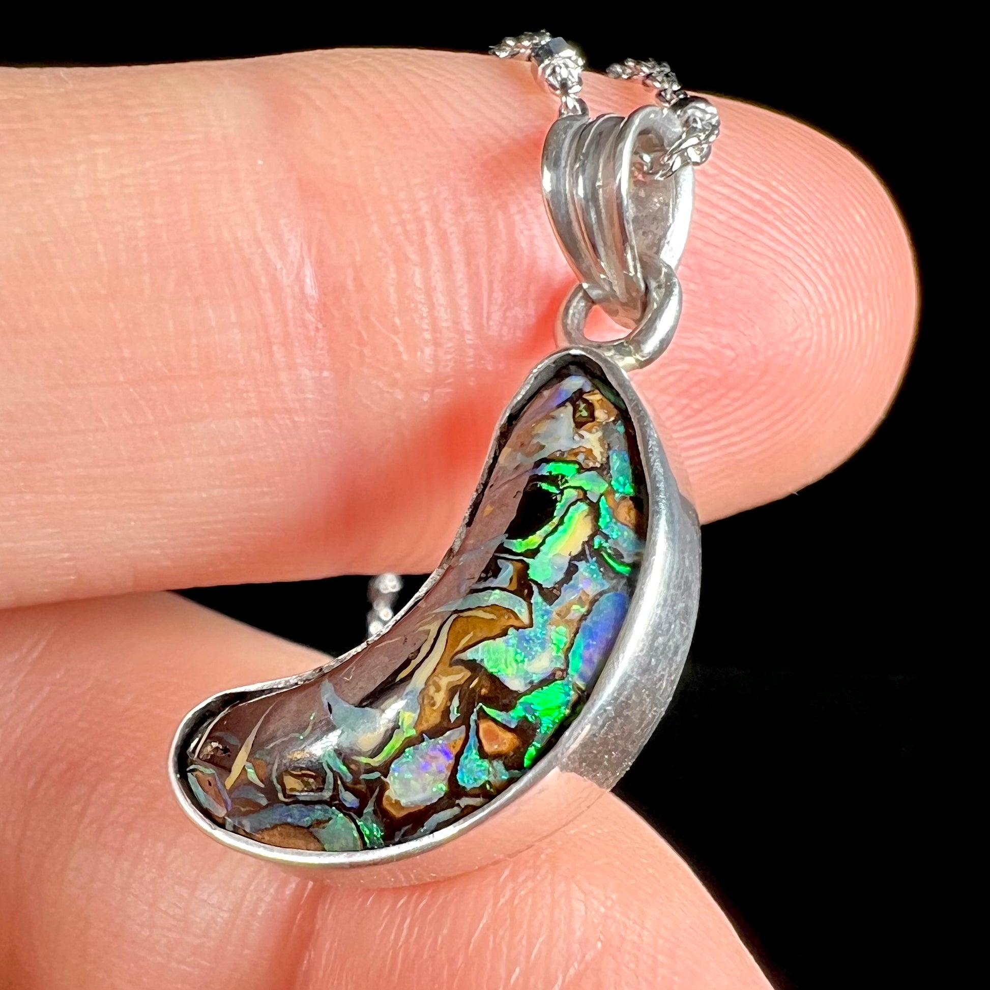 A sterling silver necklace bezel set with a natural Koroit boulder opal stone.  The stone is shaped like a crescent moon.