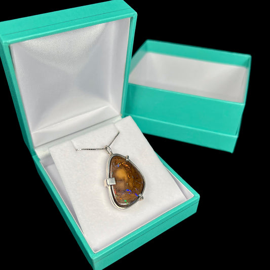 A sterling silver necklace set with a natural boulder opal.  The opal has veins of orange and blue fire.