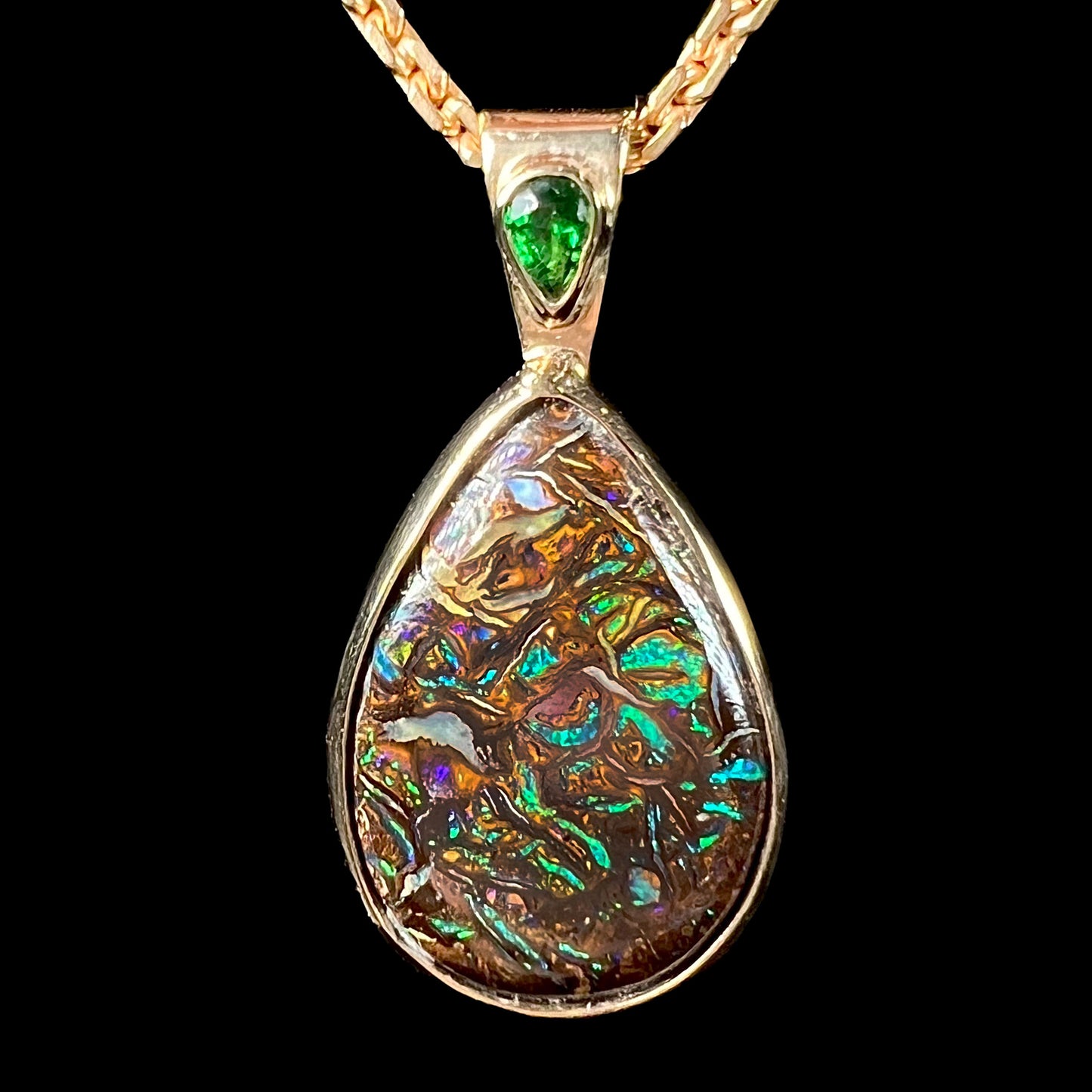 A ladies' yellow gold pendant set with a natural Koroit, Australian boulder opal and a tsavorite garnet accent stone.