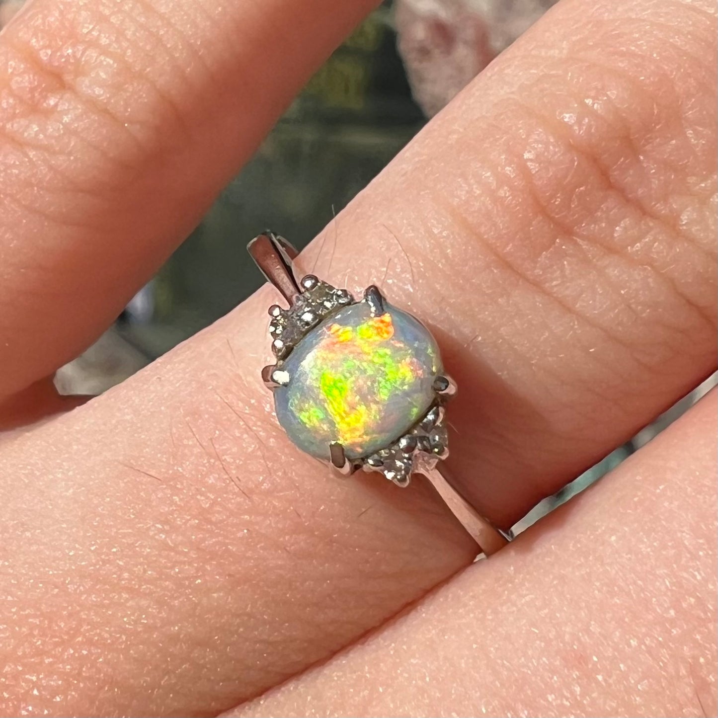 A ladies' white gold opal and diamond ring.  The opal shines orange, yellow, and green colors.