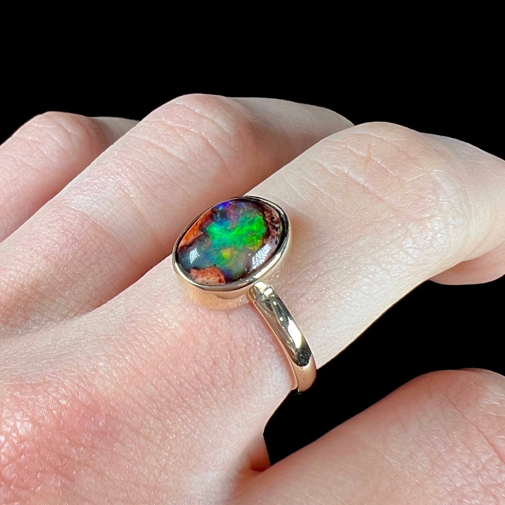 A ladies' yellow gold solitaire ring bezel set with an oval cabochon cut natural black Mexican cantera fire opal stone.