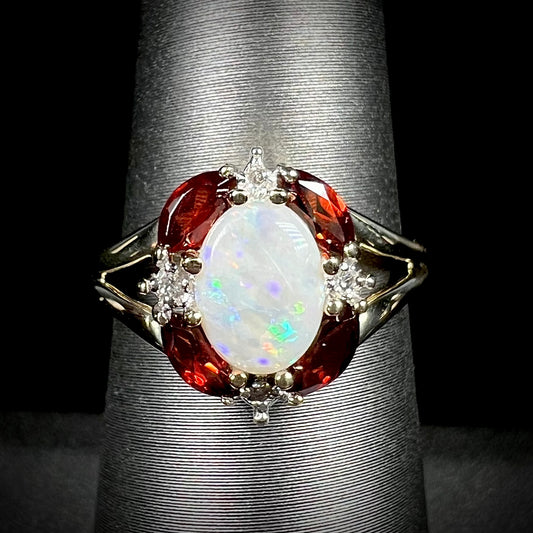 A ladies natural opal ring in yellow gold.  The opal is surrounded by red marquise cut garnets and diamonds.