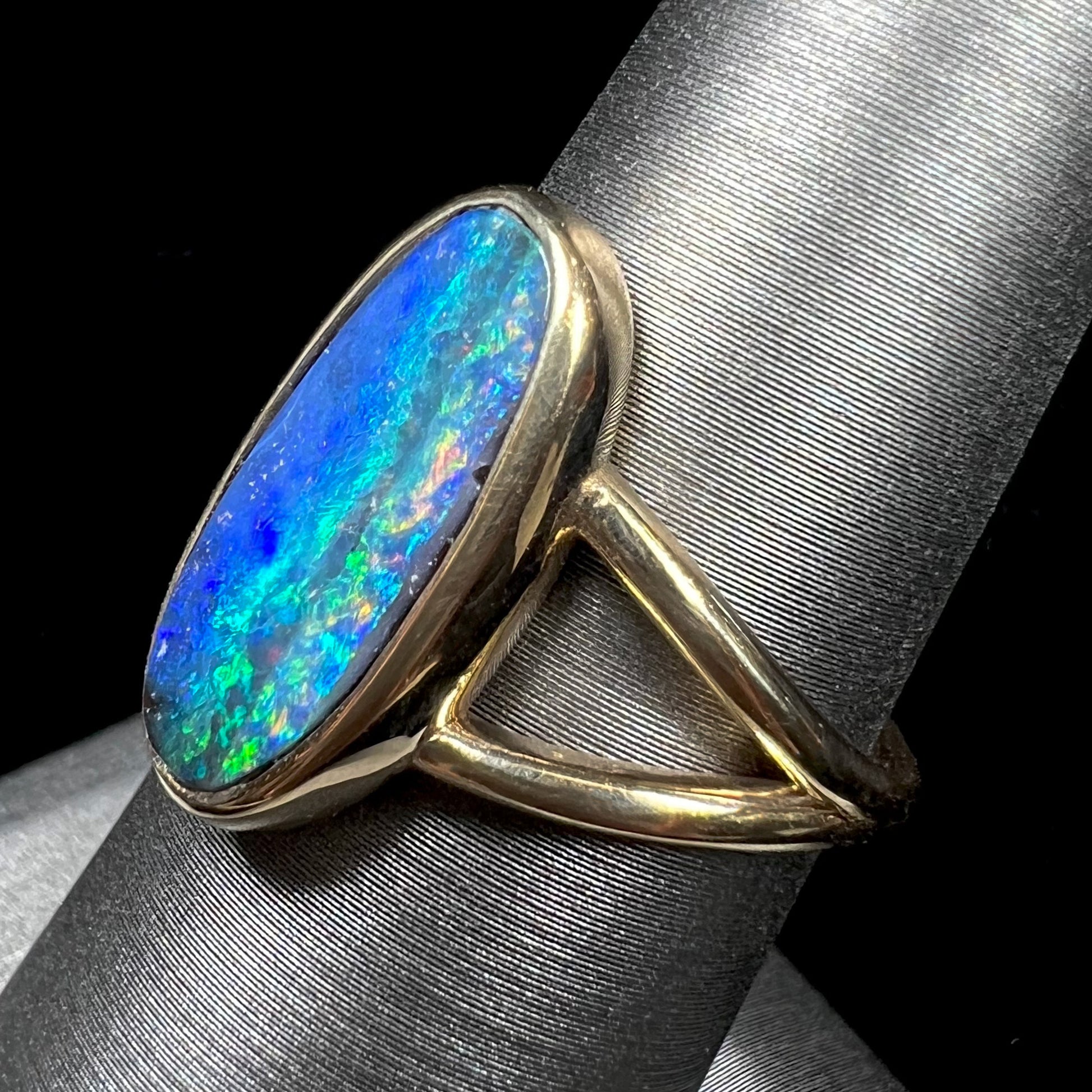 A ladies' yellow gold split shank solitaire ring set with a natural Australian black boulder opal.