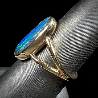 A ladies' yellow gold split shank solitaire ring set with a natural Australian black boulder opal.