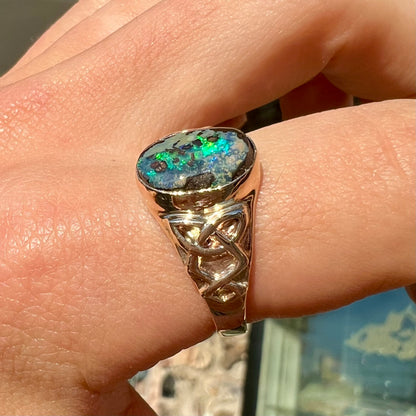 A unisex Celtic style natural boulder opal ring cast in yellow gold.  The opal shines green and blue.