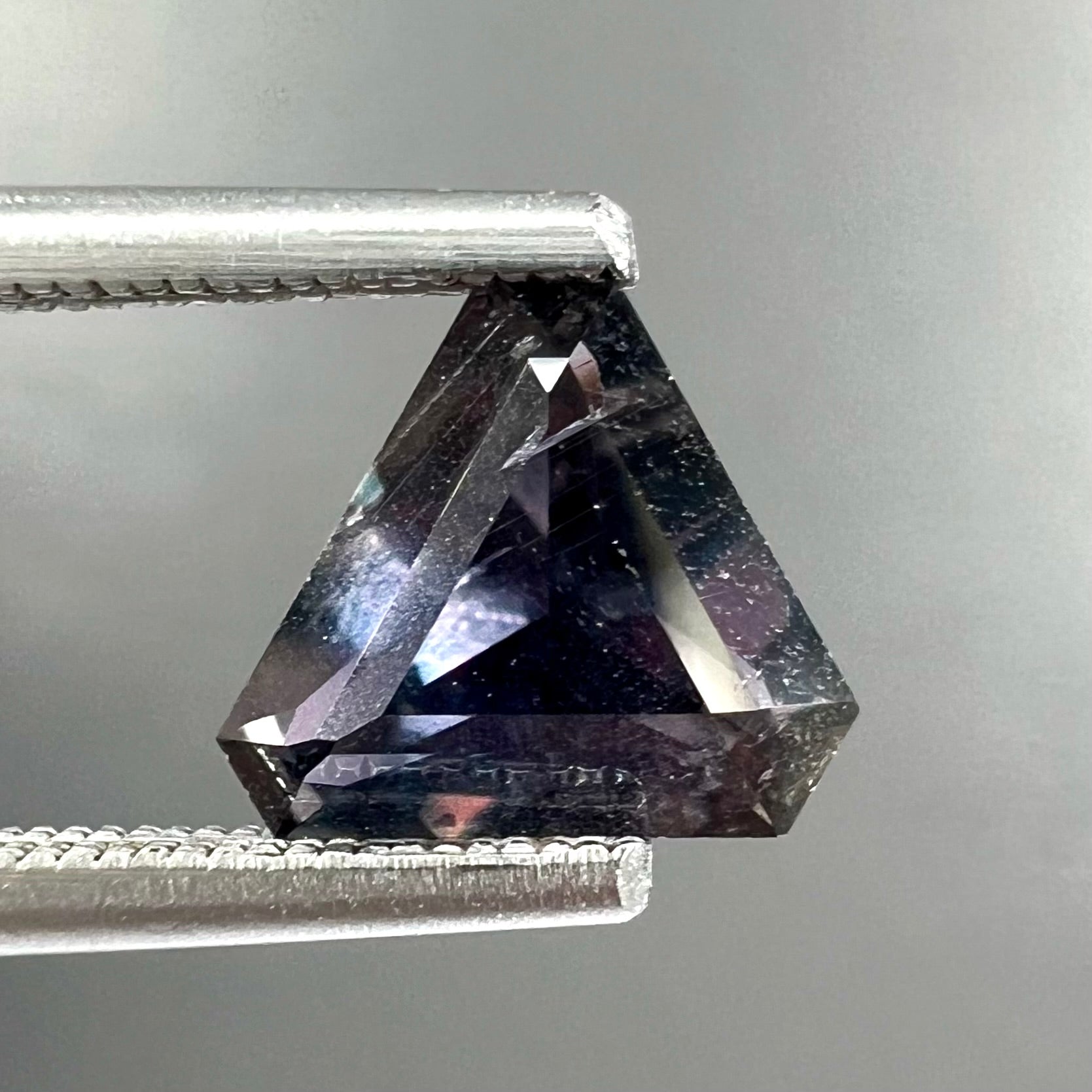 A loose, modified triangle cut parti sapphire gemstone.  The sapphire shows colors of blue, violet, purple, and gray.