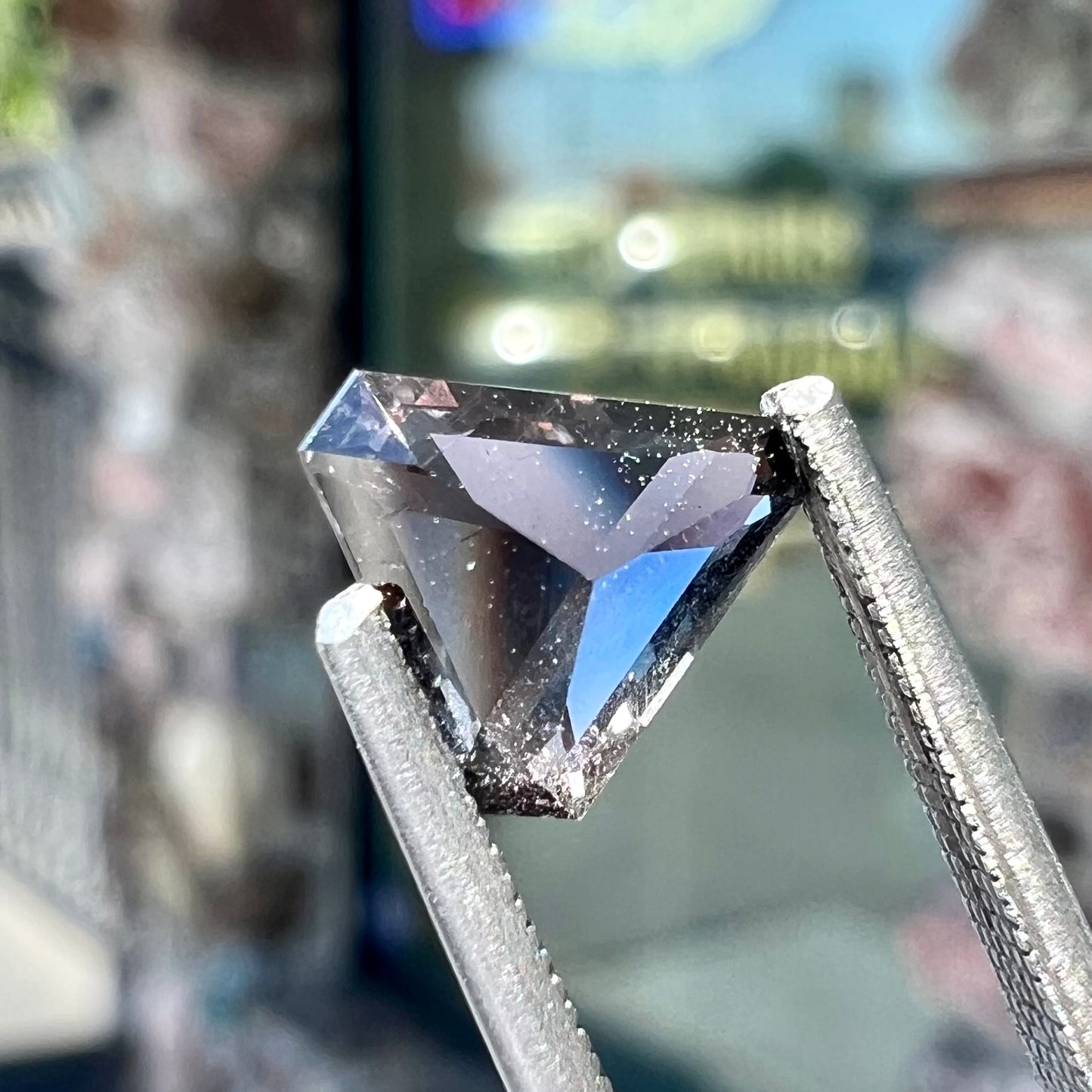 A loose, modified triangle cut parti sapphire gemstone.  The sapphire shows colors of blue, violet, purple, and gray.