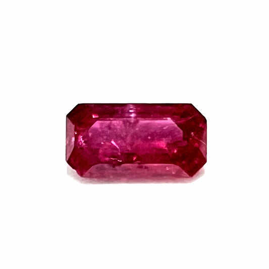 A loose, purplish red natural ruby gemstone.  The stone is emerald cut.