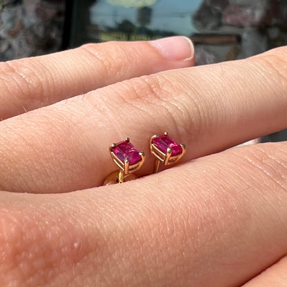 A pair of yellow gold stud earrings set with pinkish red Burmese rubies.  The rubies are emerald cut.