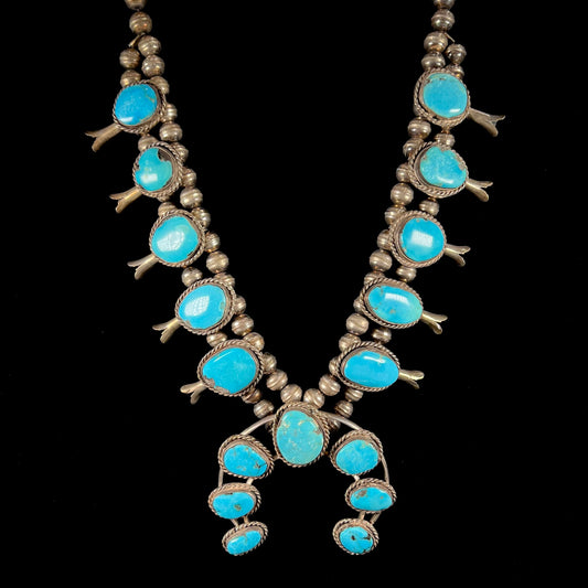A sterling silver, Navajo style squash blossom necklace set with Morenci turquoise stones.  The legnth is designed for women and children.