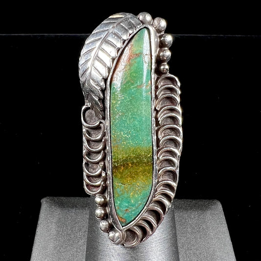 A sterling silver Navajo style ring set with a turquoise stone that shows colors of green, yellow, and reddish brown.