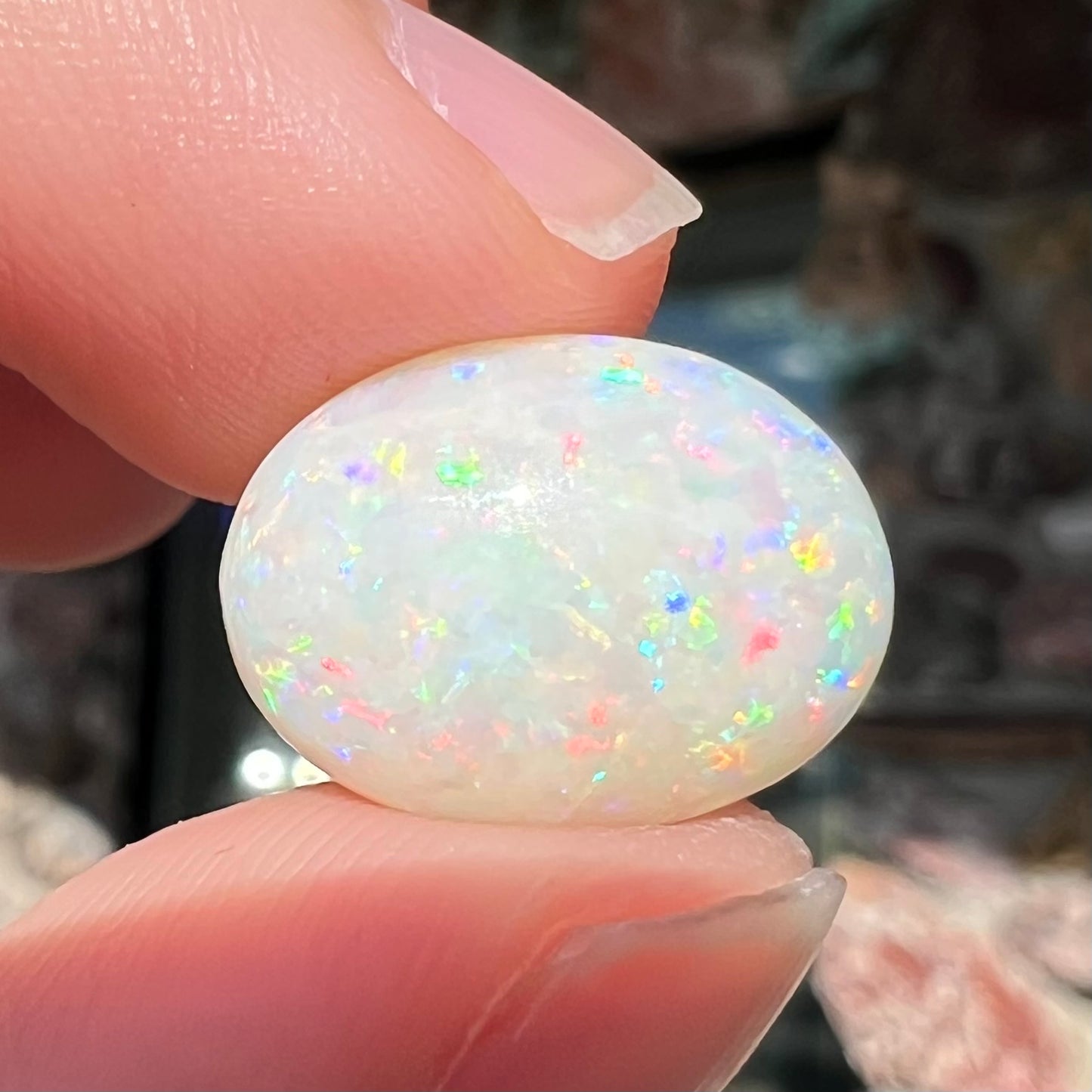 An oval cabochon cut white opal.  The opal has an eye-visible natural fissure inclusion.