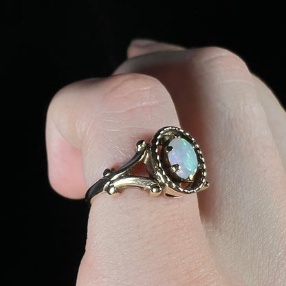 A ladies' Art Nouveau style opal solitaire ring.  The mounting is yellow gold with filigree accents.