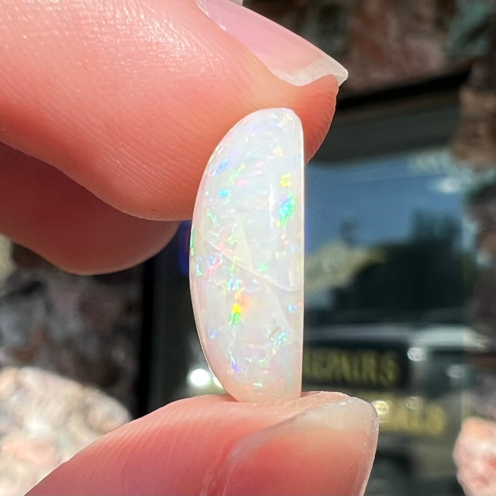An oval cabochon cut white opal.  The opal has an eye-visible natural fissure inclusion.