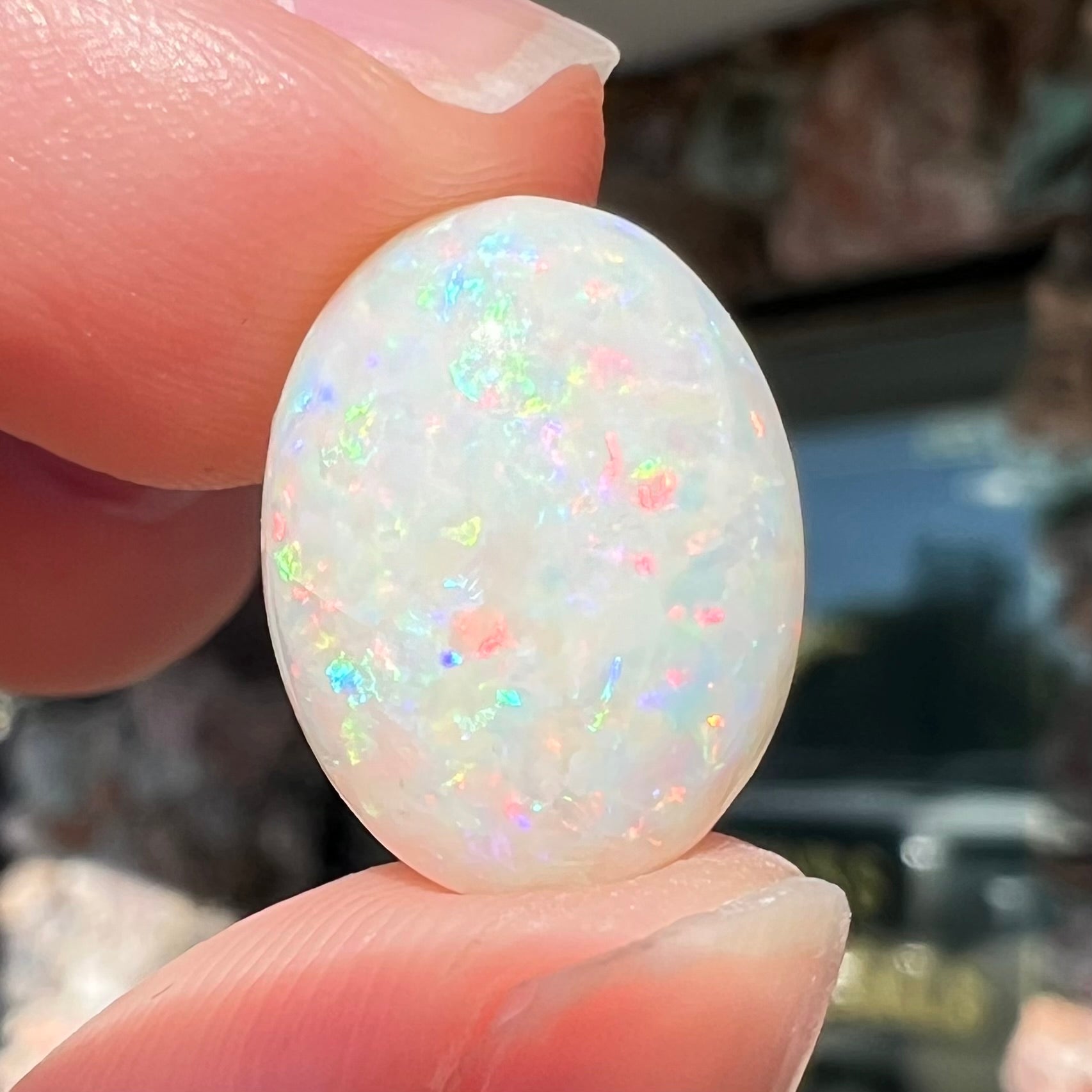 An oval cabochon cut white opal.  The opal has an eye-visible natural fissure inclusion.
