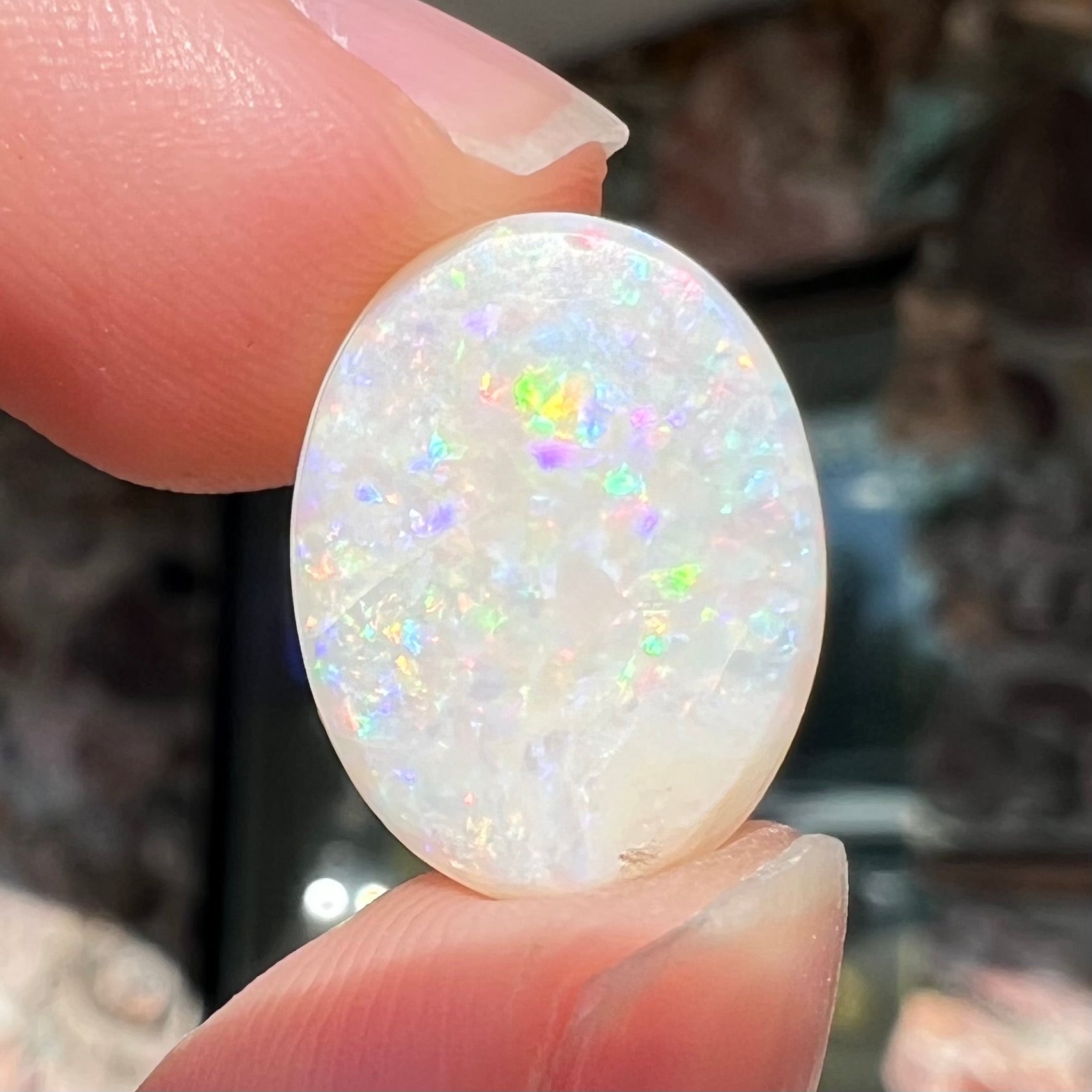 An oval cabochon cut white opal.  The opal has an eye-visible natural fissure inclusion.