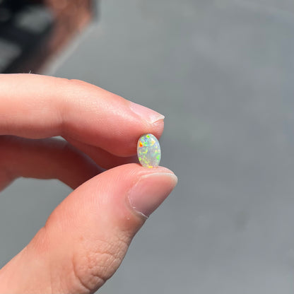 A loose, oval cabochon cut semi-black opal stone from Lightning Ridge, Australia.