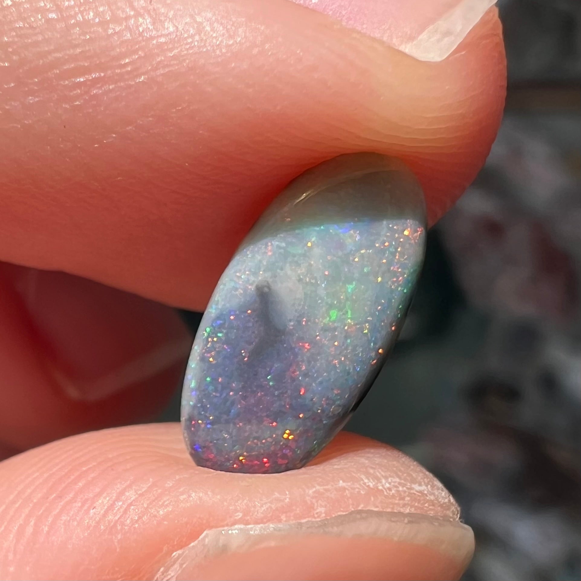 A loose, oval cabochon cut opal gemstone from Lightning Ridge, Australia.  The opal shines red and orange colors.