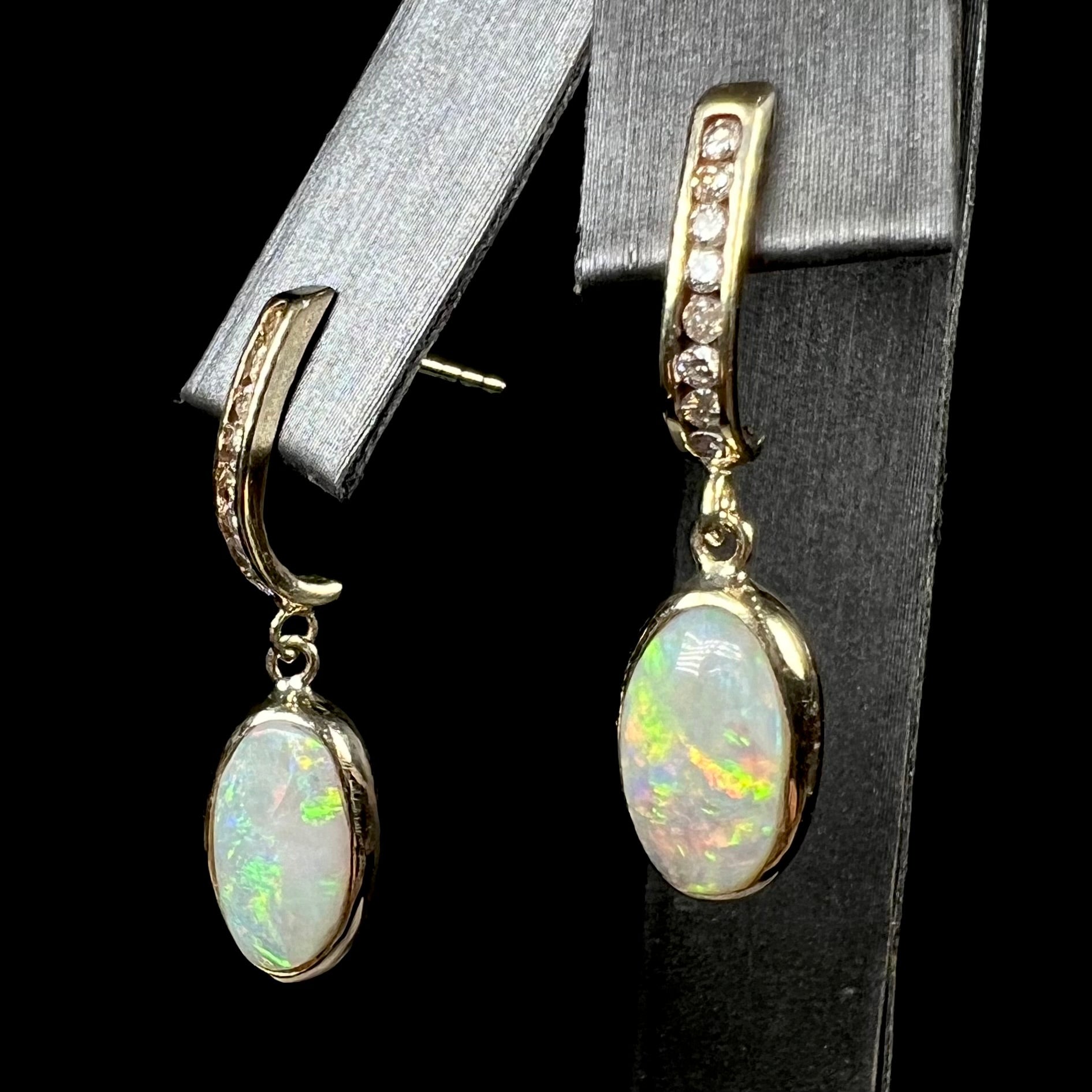 A pari of yellow gold dangle earrings set with natural white crystal opals and diamond accents.