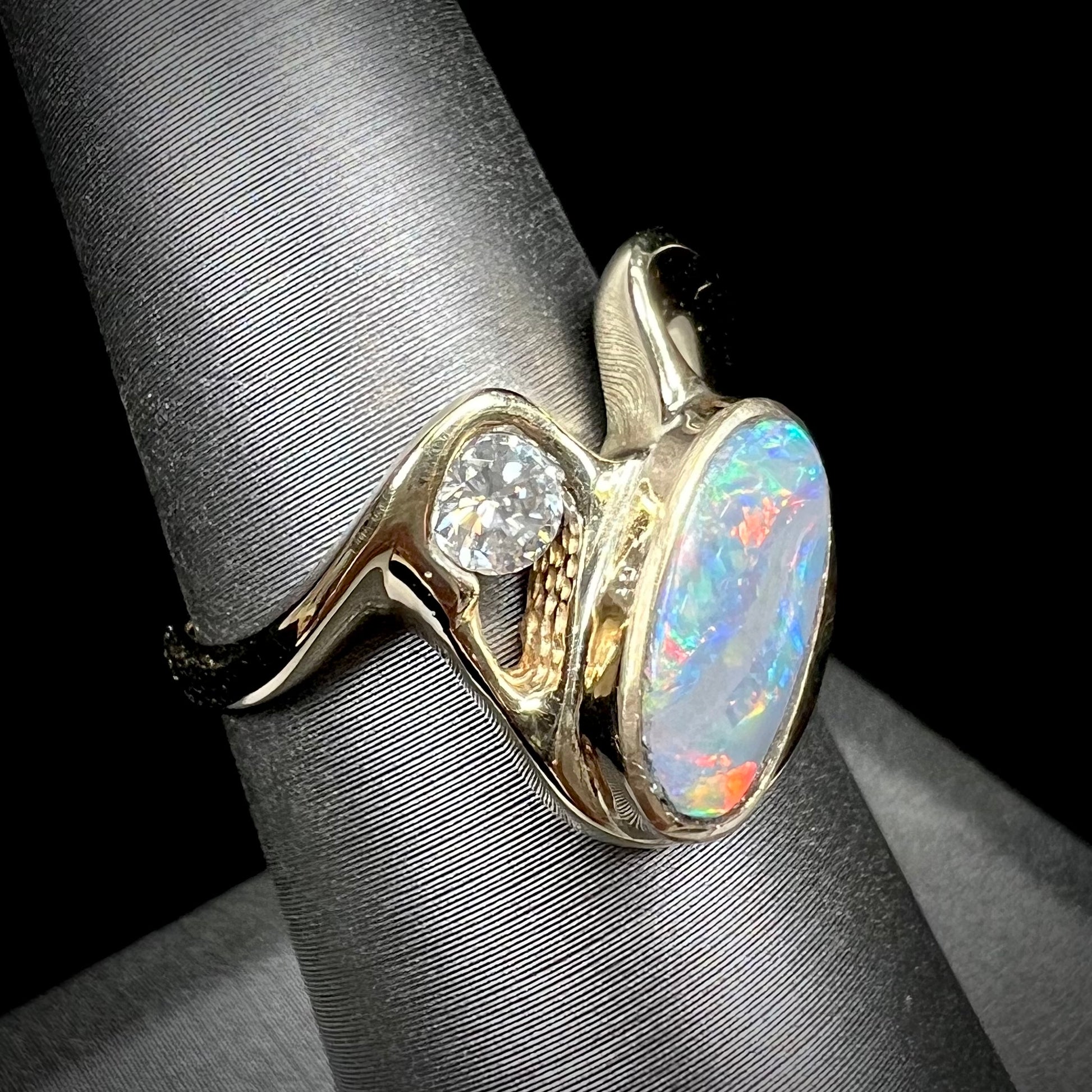 A ladies' yellow gold, bezel set ring mounted with a natural 1.15 carat black opal and round diamond.