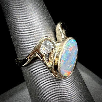 A ladies' yellow gold, bezel set ring mounted with a natural 1.15 carat black opal and round diamond.