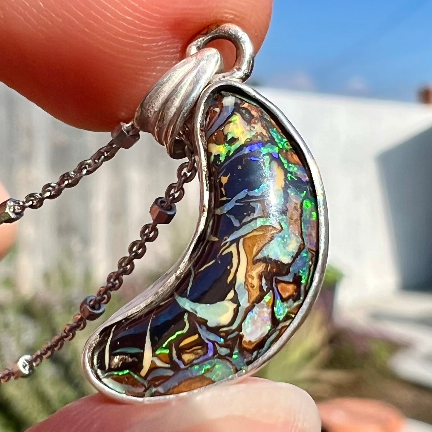 A sterling silver necklace set with a natural Koroit boulder opal shaped like a crescent moon.