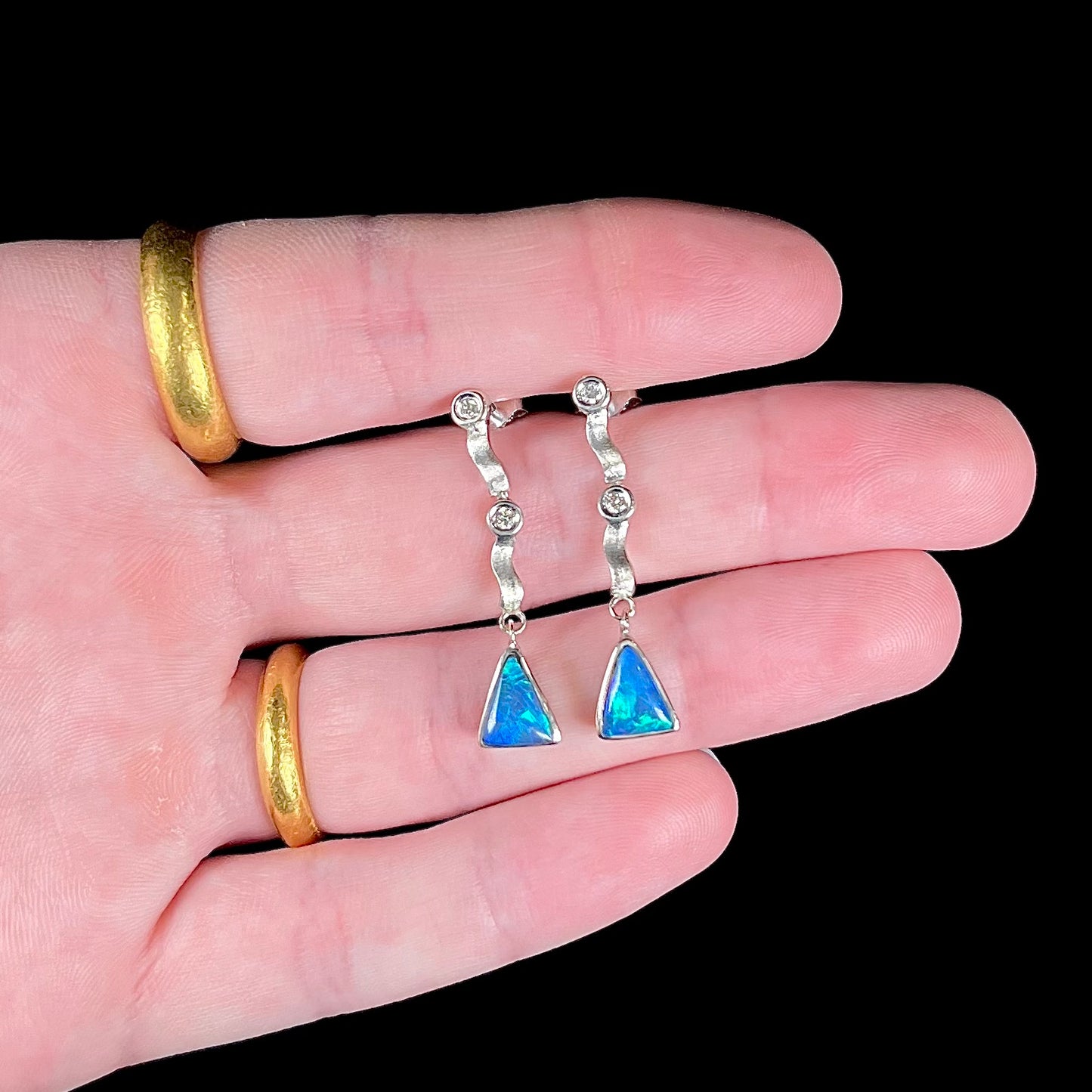 A pair of white gold earrings set with triangle cut natural black opals and round diamond accents.