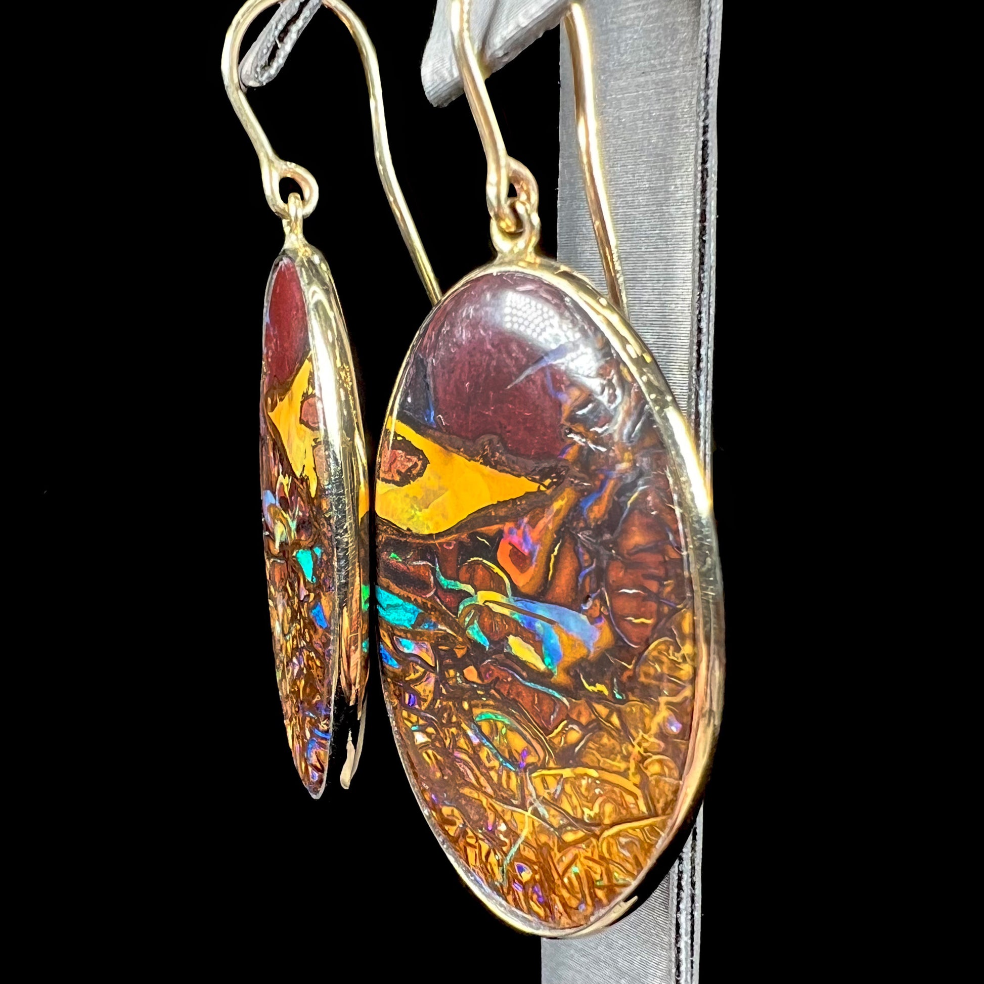 A pair of oval cut Koroit boulder opal dangle earrings in yellow gold bezel frames.  The opal exhibits a unique pattern and blue colors.