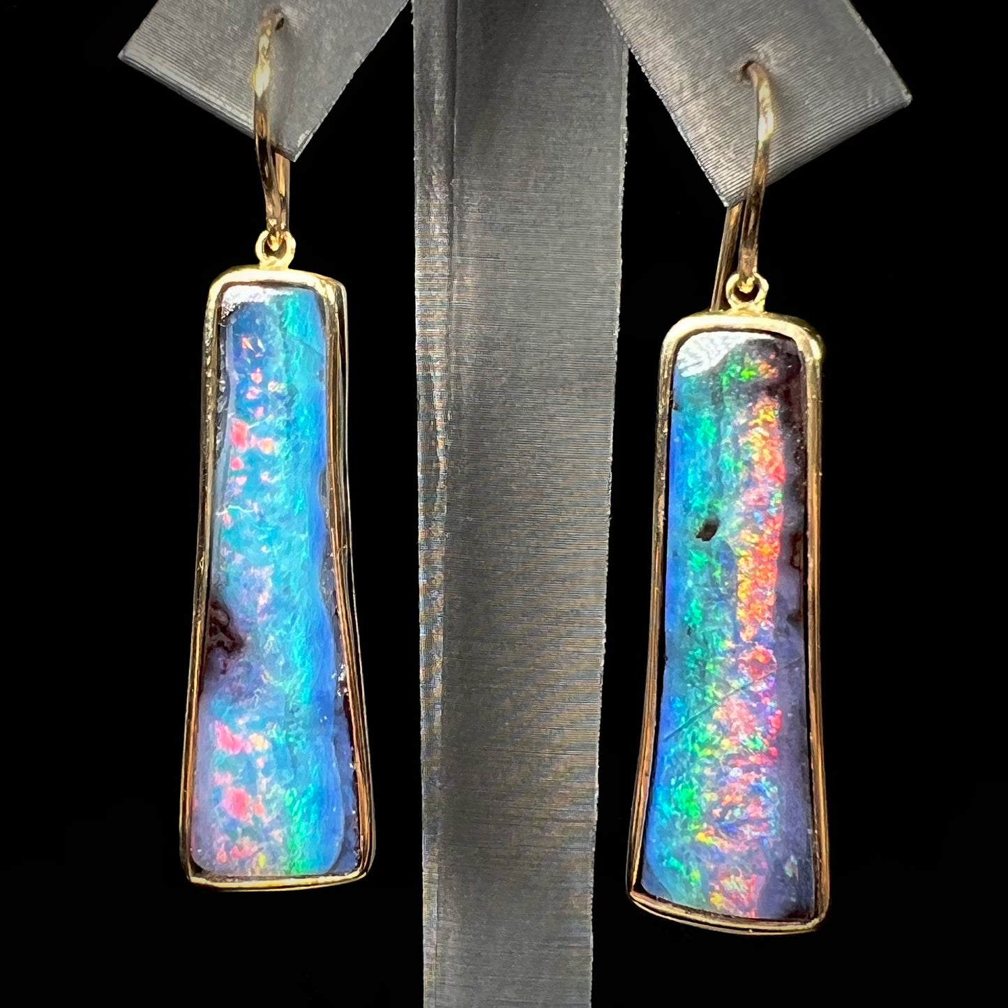 A pair of natural boulder opal dangle earrings set in yellow gold.  The opal displays a rainbow of colors and is from Bull Creek, Australia.