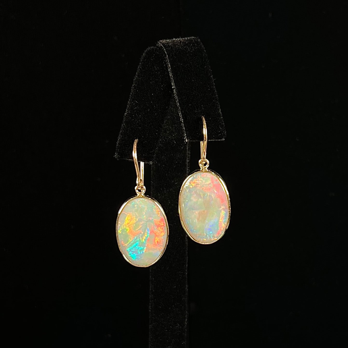 A pair of yellow gold earrings bezel set with oval cabochon cut natural opal stones.