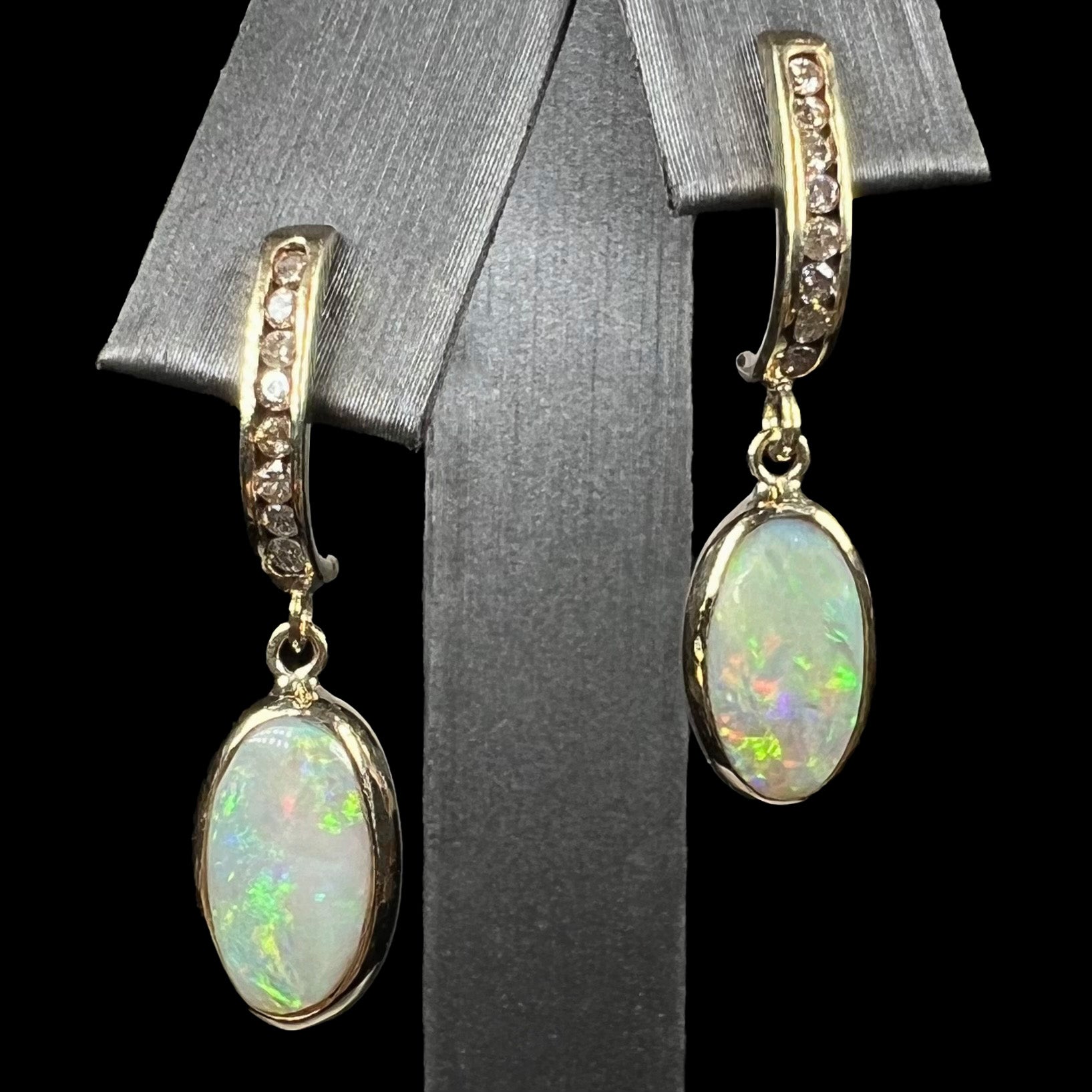 A pari of yellow gold dangle earrings set with natural white crystal opals and diamond accents.